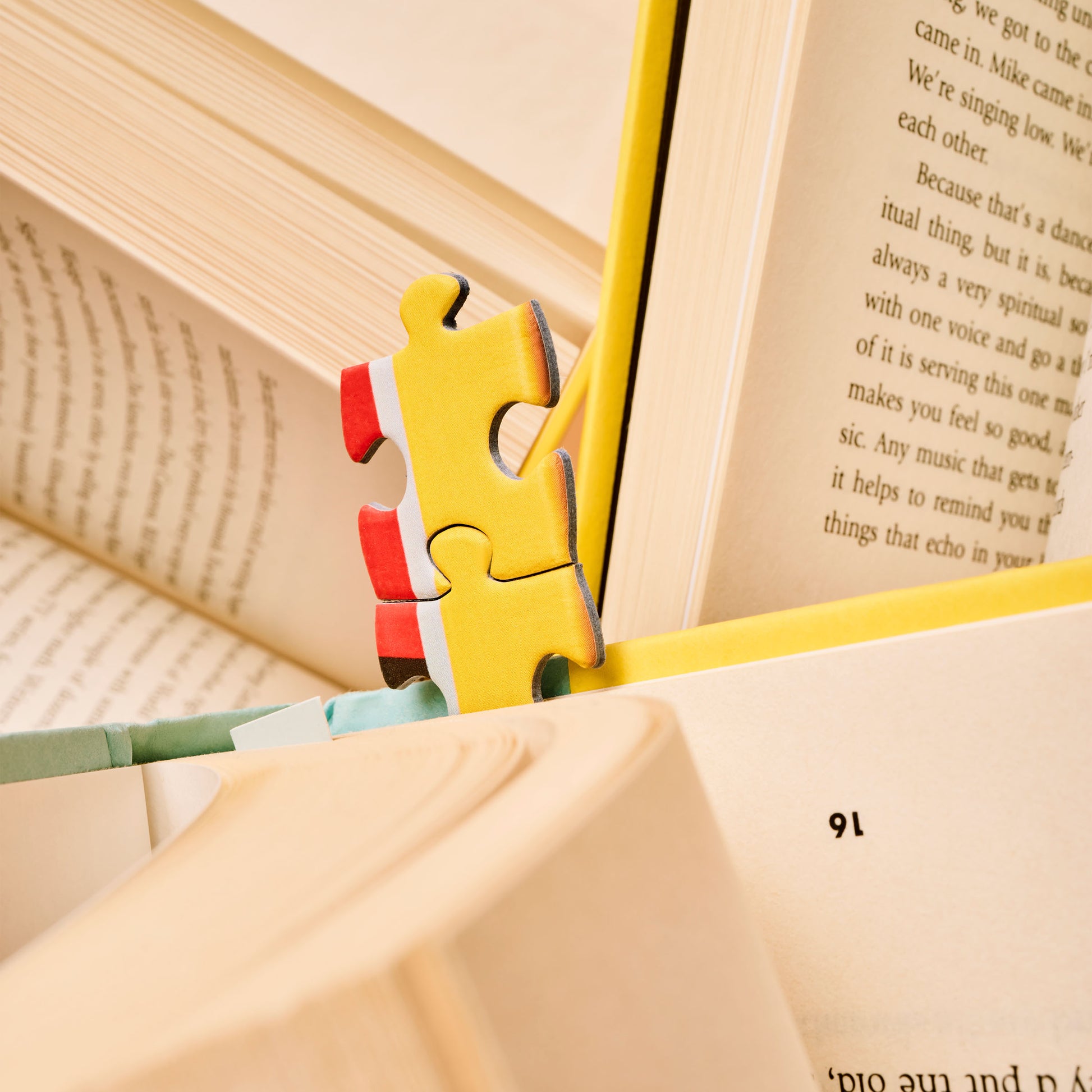 A puzzle piece from Bookworm, a 500-Piece Puzzle from Piecework Puzzles, sticking out of a book like a bookmark.