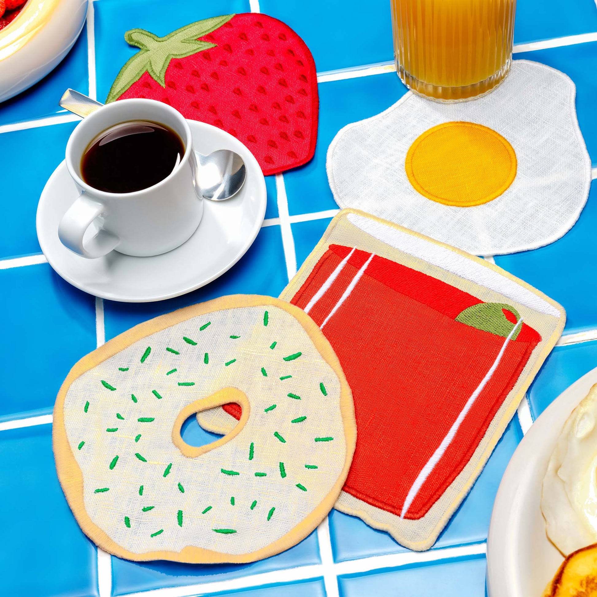 Brunch-themed cocktail napkins by Piecework featuring a bagel, egg, strawberry, and bloody mary—styled with breakfast tableware.