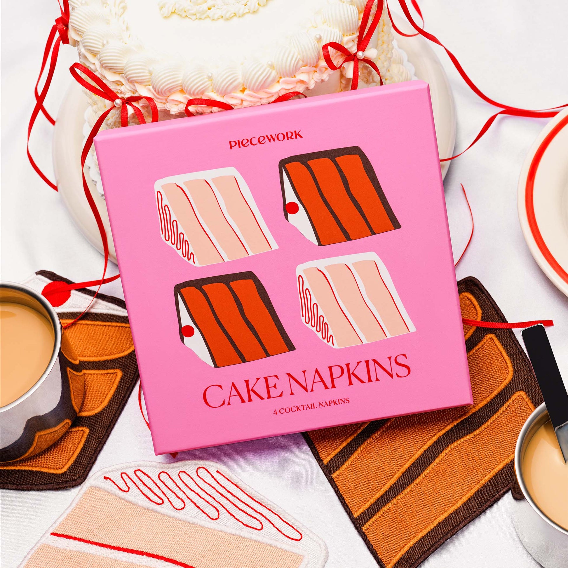 Piecework Cake Napkins boxed gift set with slices of classic layer cake-shaped linen cocktail napkins styled alongside coffee and celebration cake.