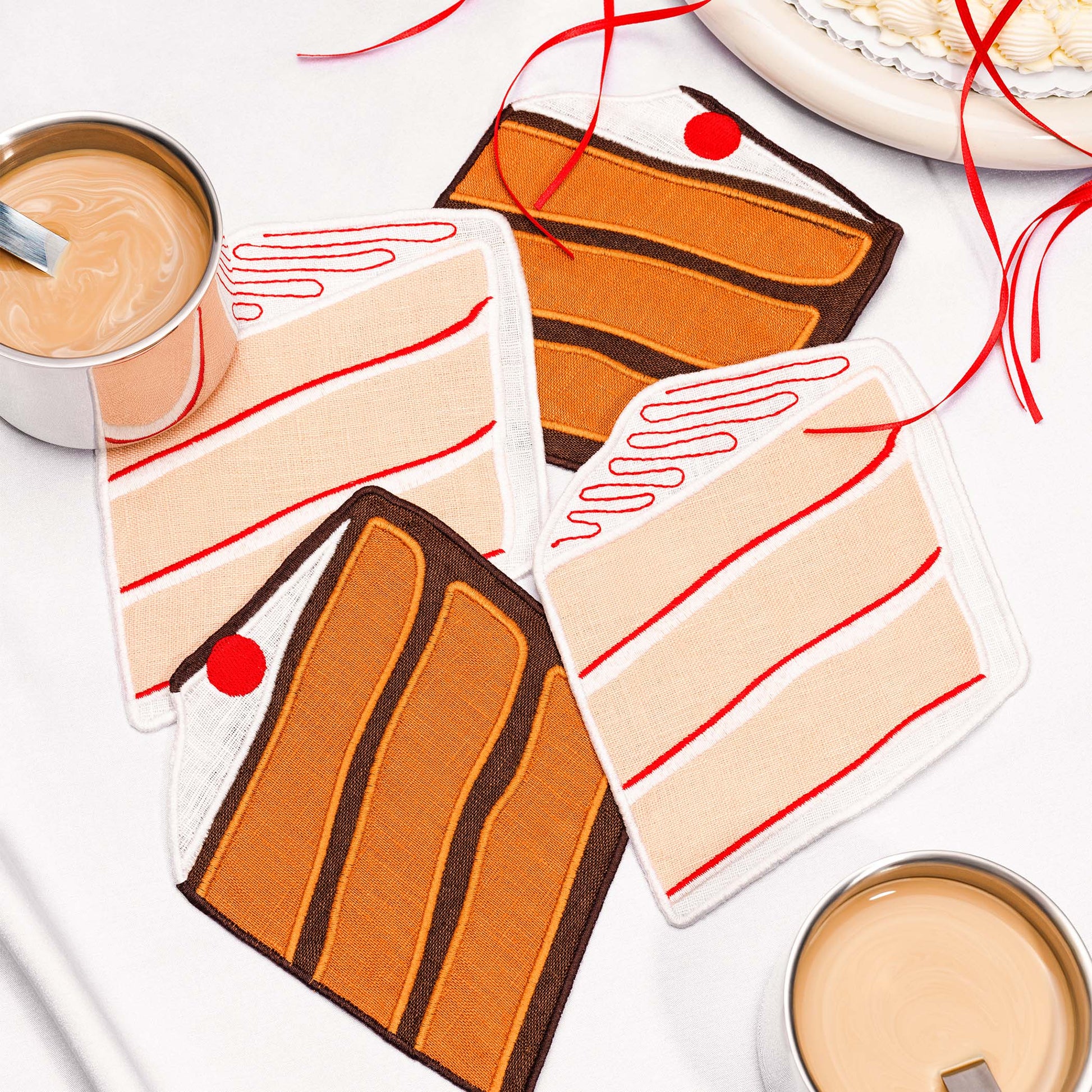 Cake slice-shaped cocktail napkins by Piecework styled with coffee, frosting ribbons, and dessert—perfect for birthdays and sweet gifting.