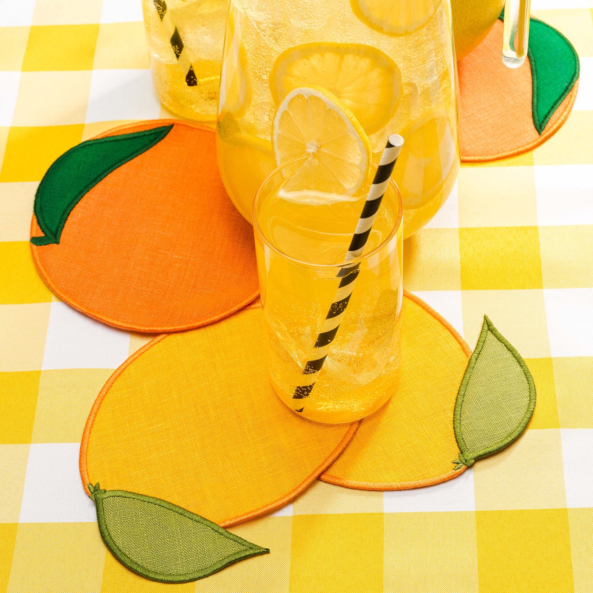Citrus-shaped linen cocktail napkins by Piecework styled with lemonade and lemon slices on a yellow gingham tablecloth.
