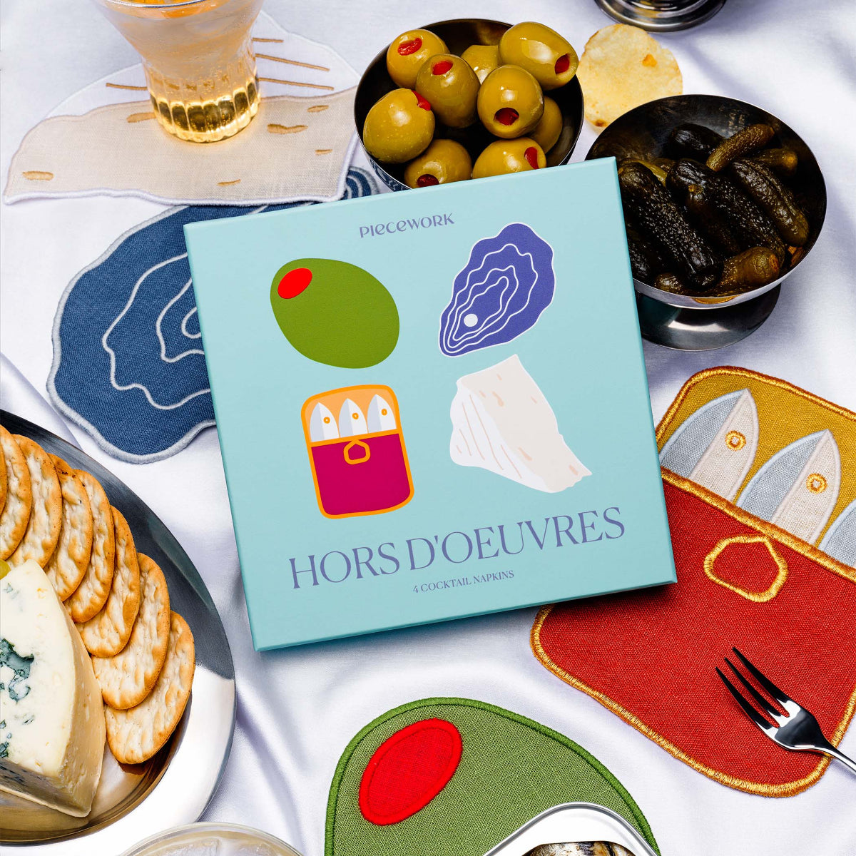 Piecework Hors d’Oeuvres Napkins boxed gift set with 100% linen themed cocktail napkins styled with olives, cheese, and drinks.