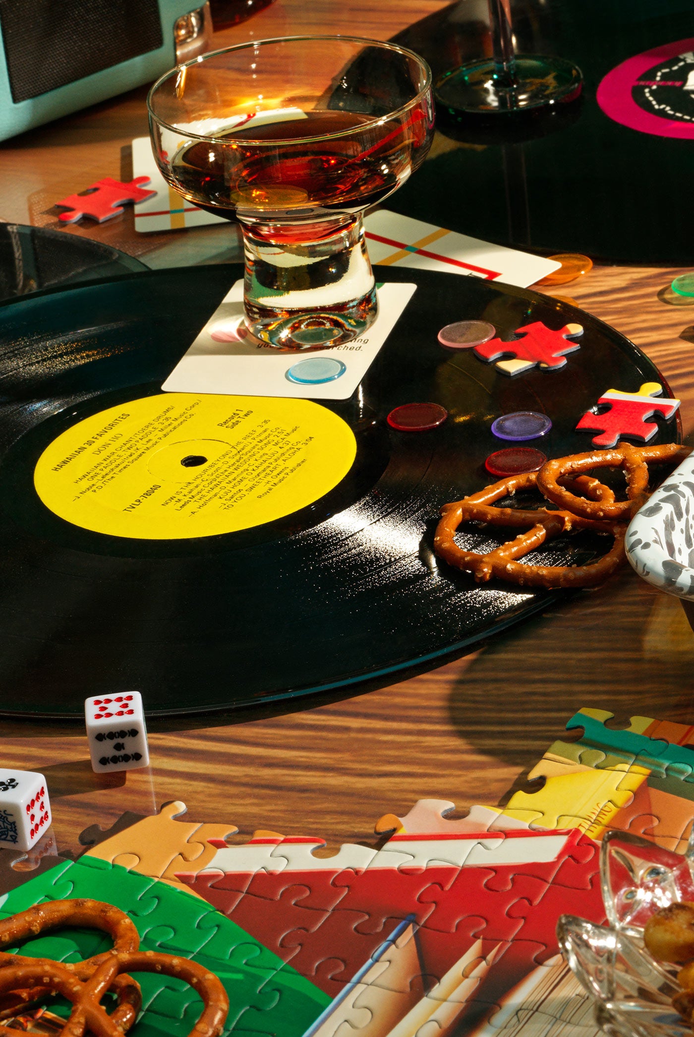 A table scene featuring a record player, cocktails and a puzzle tray filled with puzzle pieces.