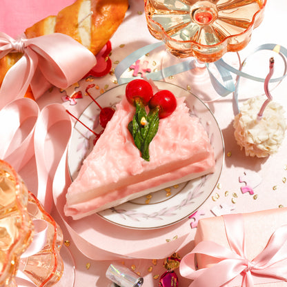 A Cherry Cake Slice Candle on a dessert plate on a celebratory table scene.