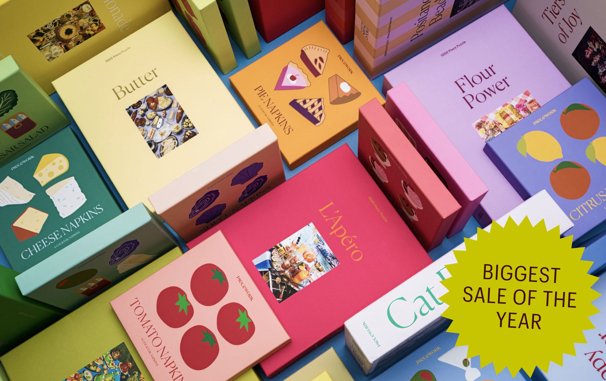 An image of boxes of Piecework puzzles and cocktail napkins with a badge labeled "BIGGEST SALE OF THE YEAR"