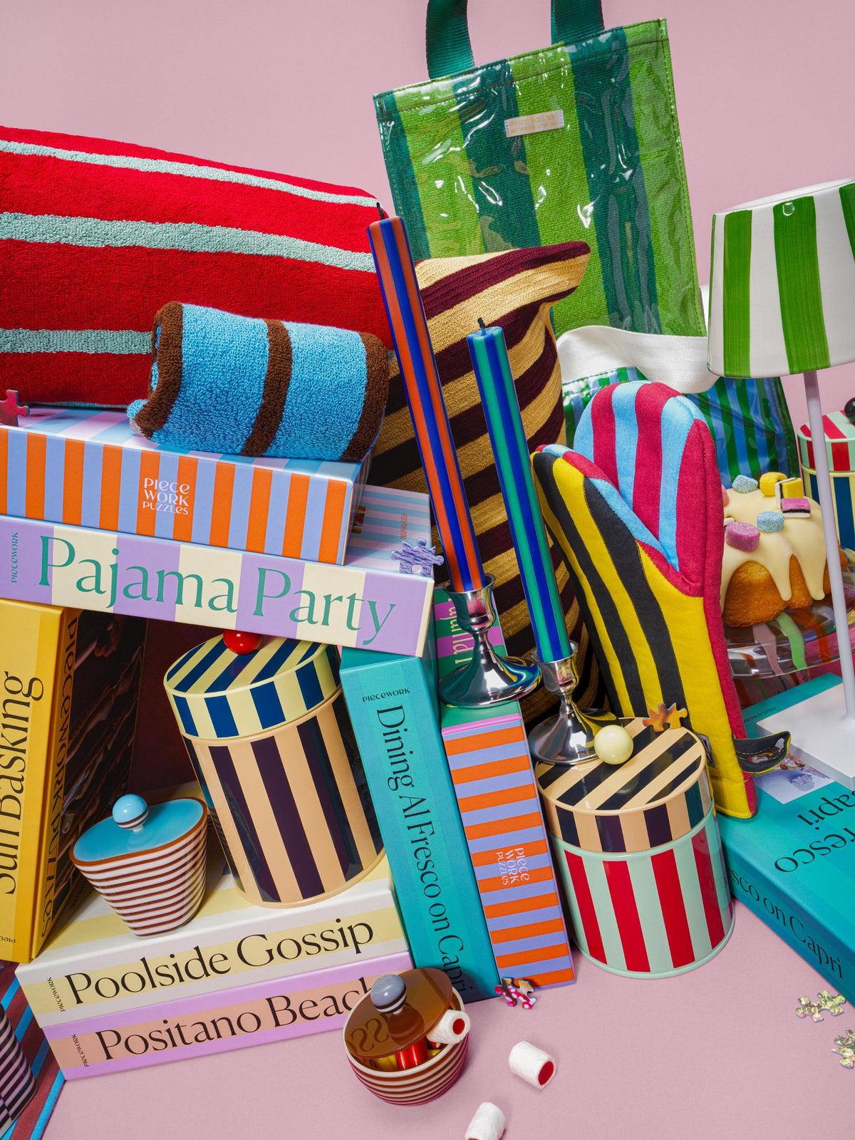 Piecework striped puzzles, candles and canisters piled beside a green mesh tote bag on pink.