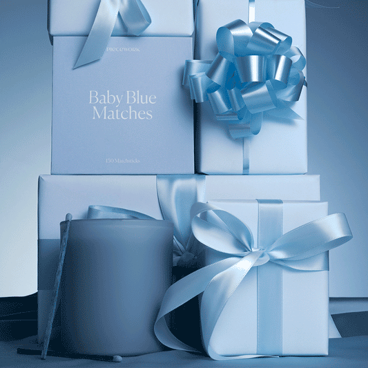 Blue candle and matches surrounded by blue gift boxes and ribbons on a matching background. The animated GIF shows a match lighting a candle with packaging for Piecework's Baby Blue Matches in the background.
