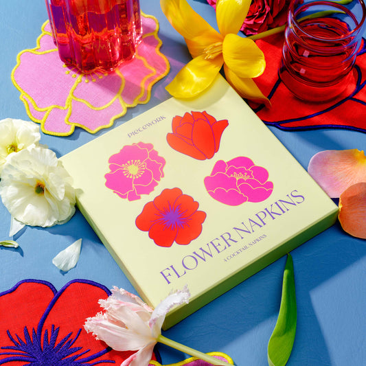 Piecework Flower Napkins boxed gift set with floral-shaped linen cocktail napkins, styled with fresh flowers and colorful glassware.