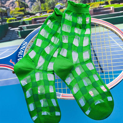 Sheer green gingham socks held up with a tennis racket with a court in the background.

