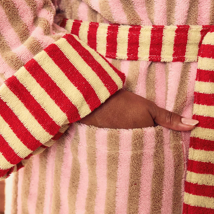 Holiday gifts from The Holiday Shop: a pink and red striped terry bathrobe, a red tartan Yahtzee Bookshelf Edition game set, gray cashmere gloves with black hearts worn with a red sweater, and a red and pink needlepoint bow ornament.