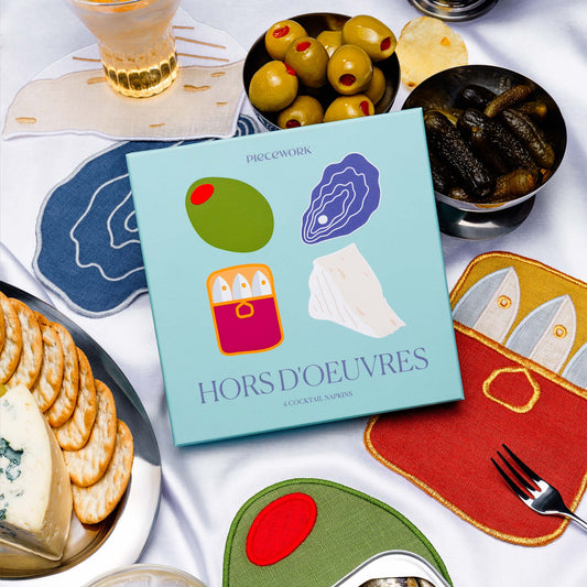 Piecework Hors d’Oeuvres Napkins boxed gift set with 100% linen themed cocktail napkins styled with olives, cheese, and drinks.