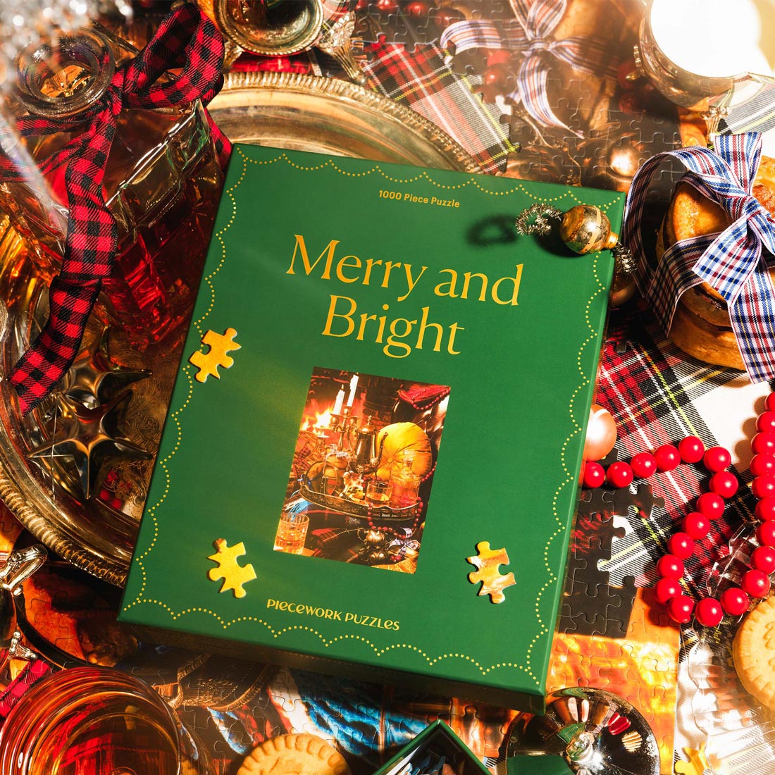Jigsaw puzzle box titled 'Merry and Bright' surrounded by plaids and other festive Christmas decorations.