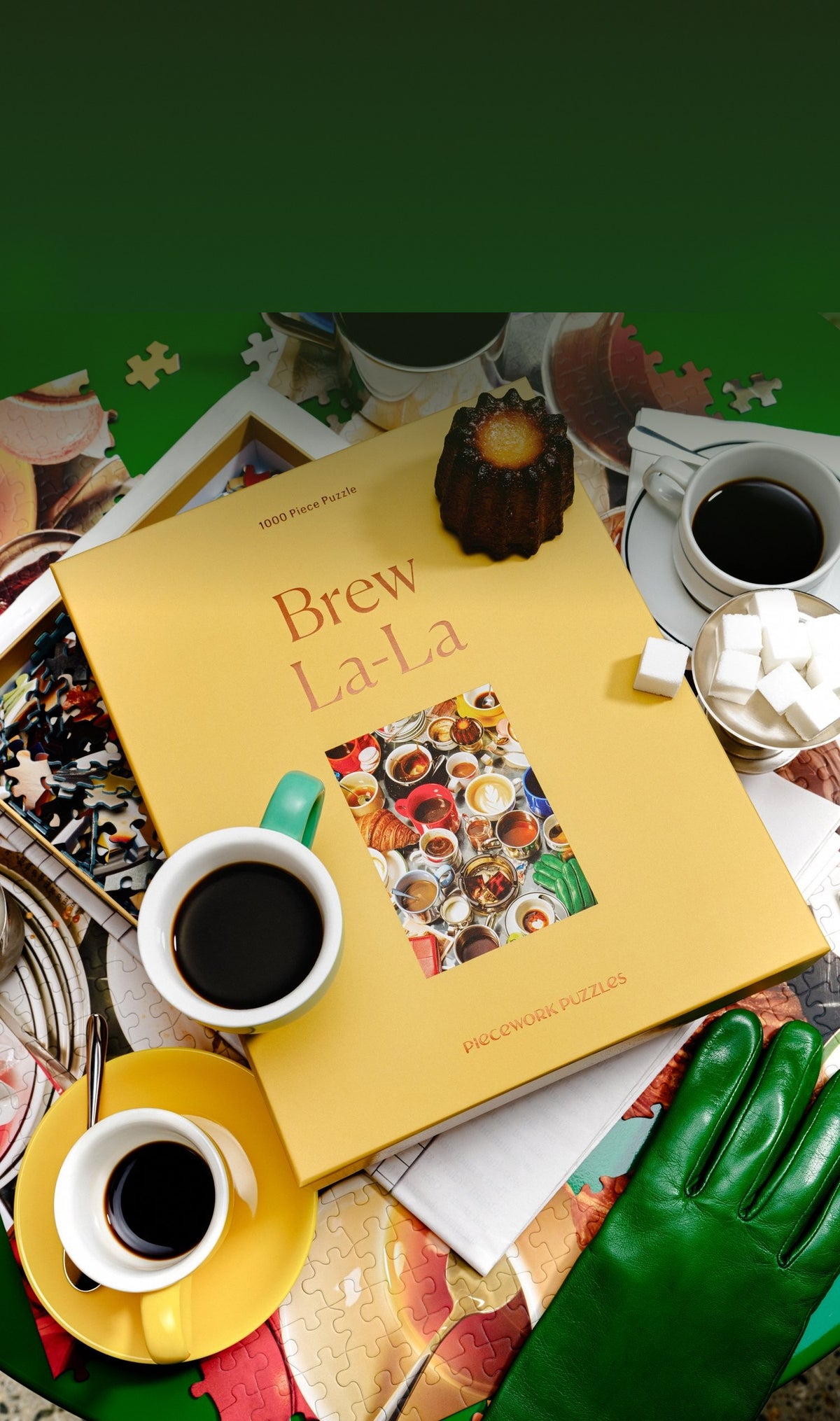 Overhead view of the Brew La-La puzzle box with cups of black coffee, sugar cubes, a canelé, and a green leather glove