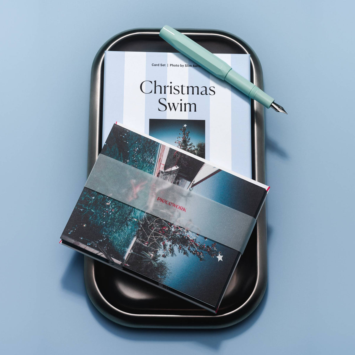 Piecework Christmas Swim Stationery Set: striped box on a black tray with banded notecards and a mint fountain pen