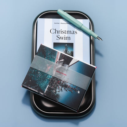 Piecework Christmas Swim Stationery Set: striped box on a black tray with banded notecards and a mint fountain pen