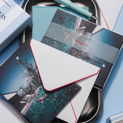 Piecework Christmas Swim Stationery Set: Slim Aarons notecard and envelope over banded cards on a tray, pale blue