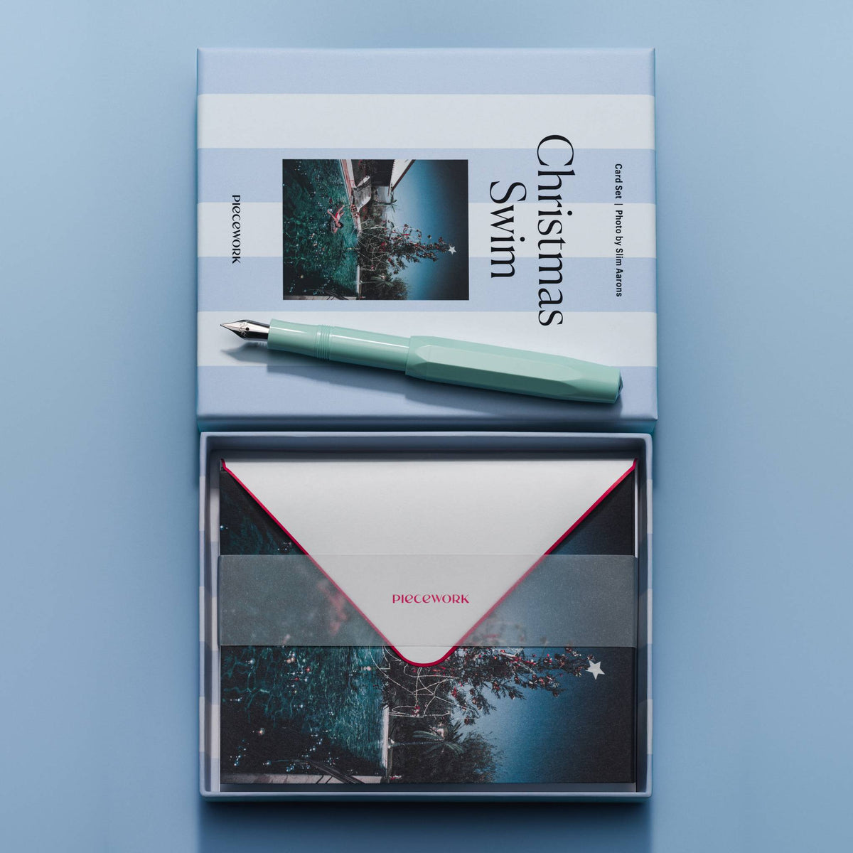 Piecework Christmas Swim Stationery Set: open box of envelopes under a vellum band below the striped lid and a mint pen