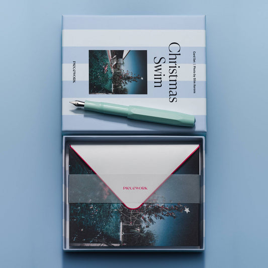 Piecework Christmas Swim Stationery Set: open box of envelopes under a vellum band below the striped lid and a mint pen