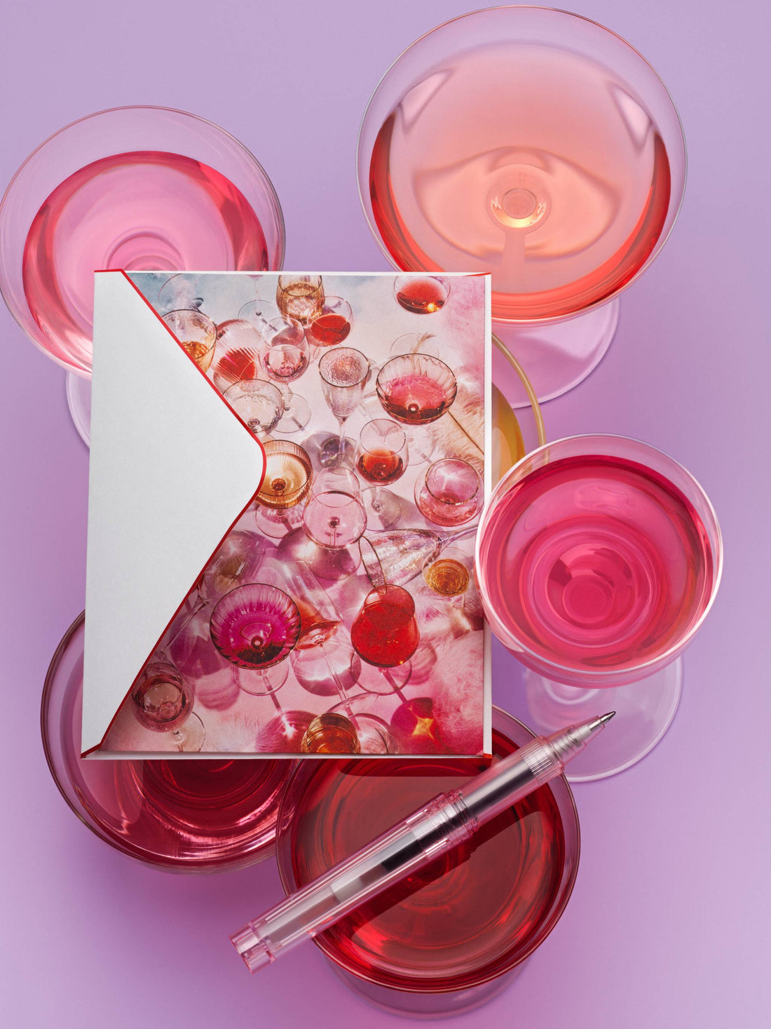 Piecework Cloud Nine notecard of pink champagne glasses with envelope and clear pen among rosé glasses on lilac