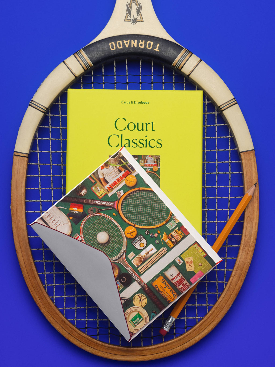 Piecework Court Classics boxed notecard set in chartreuse with tennis-themed cards on a vintage wooden racket, cobalt background