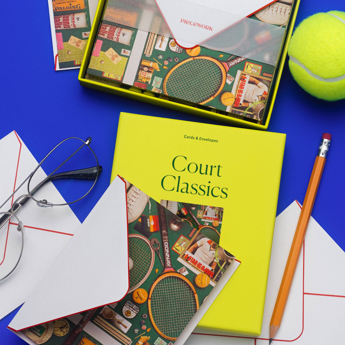 Piecework Court Classics Stationery Set: open box, notecards and envelopes with a tennis ball and eyeglasses on cobalt