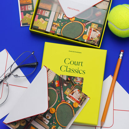 Piecework Court Classics Stationery Set: open box, notecards and envelopes with a tennis ball and eyeglasses on cobalt