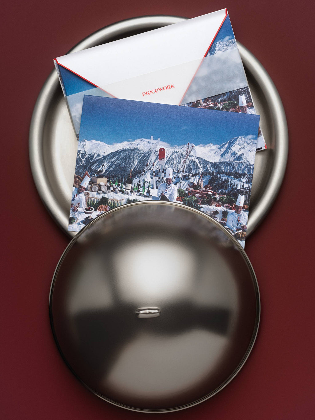 Piecework Culinary Heights notecards with an alpine feast photo and red-edged envelope on a silver tray with cloche, oxblood background