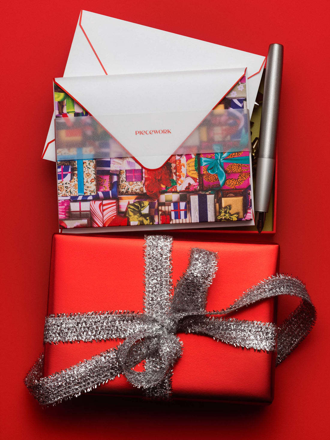Piecework Fa La La La La notecards with an envelope above a red gift wrapped in silver ribbon on red