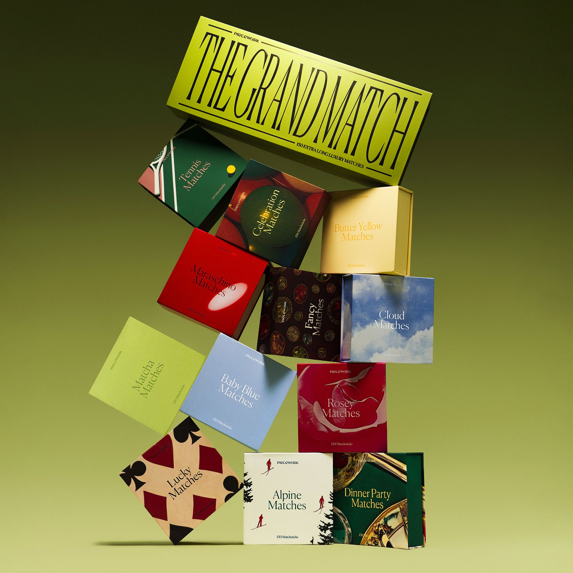 Piecework Matches Collection: A lineup of statement-making matchboxes arranged in a tower on a green background. The tower elegantly features The Grand Match, a box of extra-long luxury matches at the top.