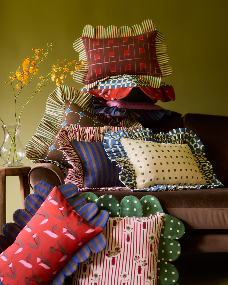 Piecework petal, ruffle and scalloped pillows piled on a brown velvet sofa beside a vase of yellow orchids