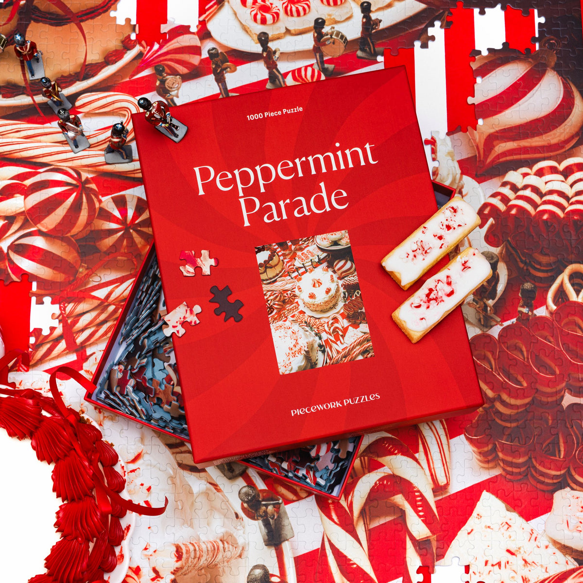 Peppermint Parade puzzle box resting on the finished red-and-white candy puzzle, with toy soldiers and frosted cookies