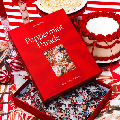Open Peppermint Parade 1000-piece puzzle box with loose pieces beside a red-frosted cake and candy-striped ornaments