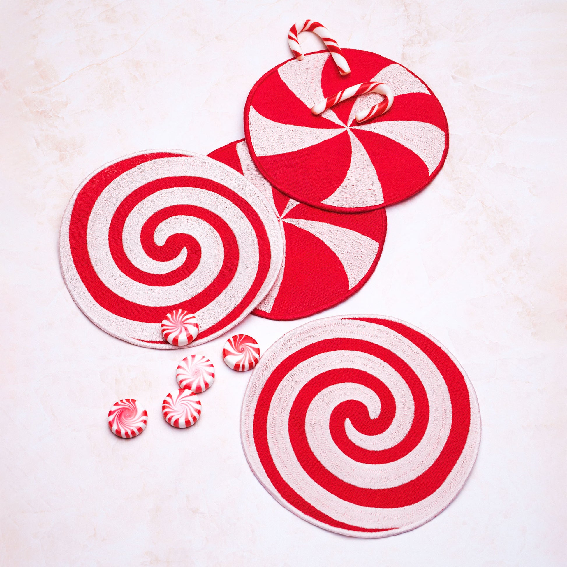 Red and white spiral peppermint linen coasters with candy canes and peppermints on a light background.