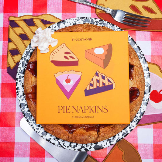Pie Napkins packaging placed on top of a baked pie on top of a red gingham tablecloth and linen pie napkins.