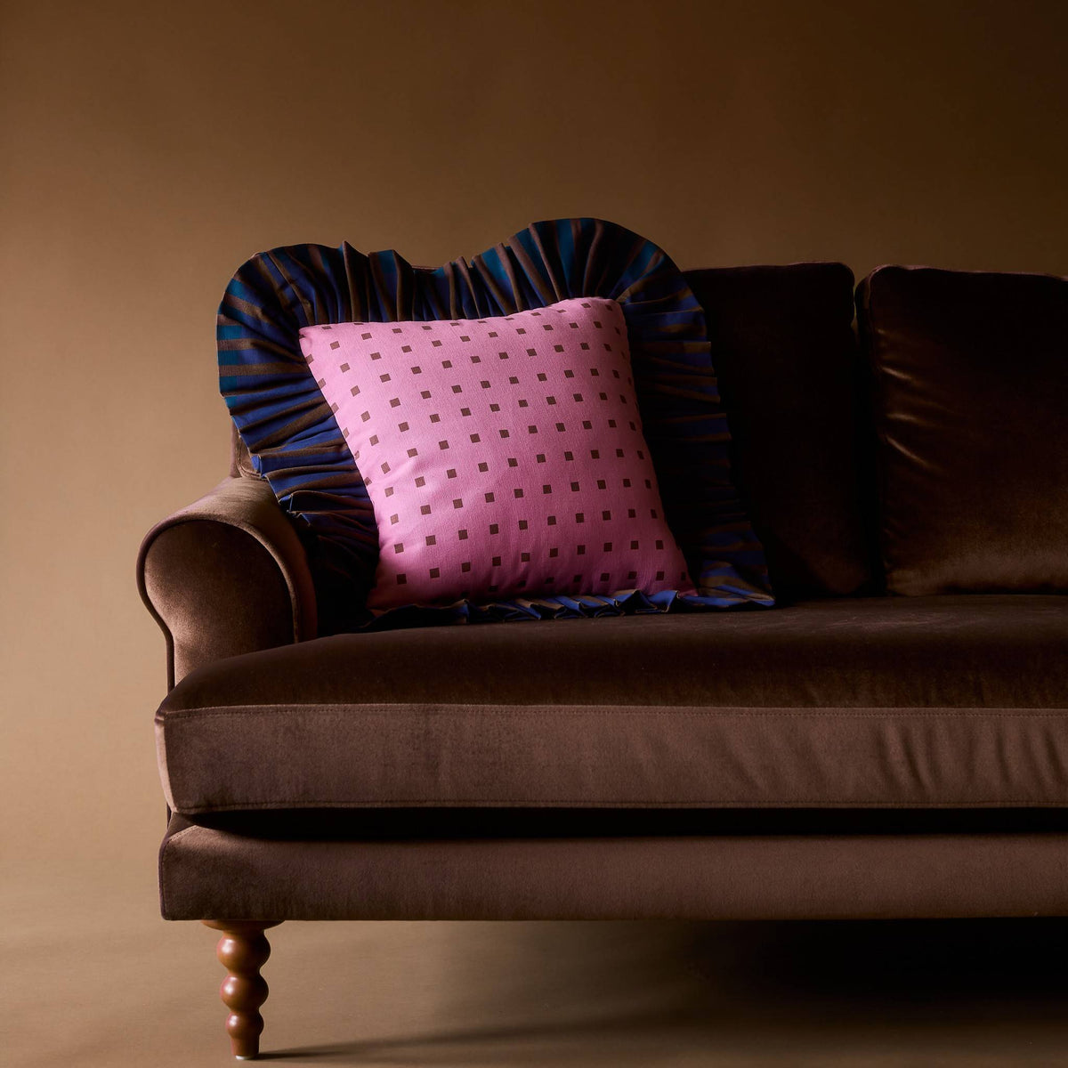Pink Checks Ruffle Pillow on a brown velvet sofa