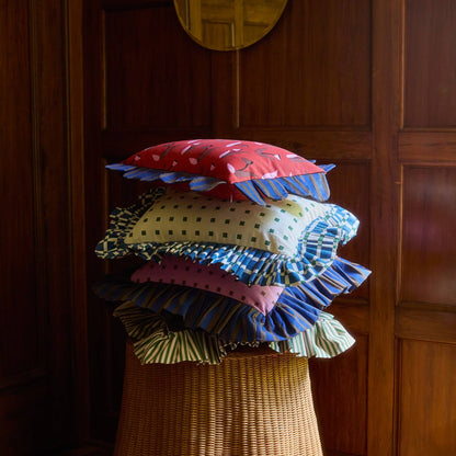 Pink Checks Ruffle Pillow in a stack of Piecework pillows on a wicker table