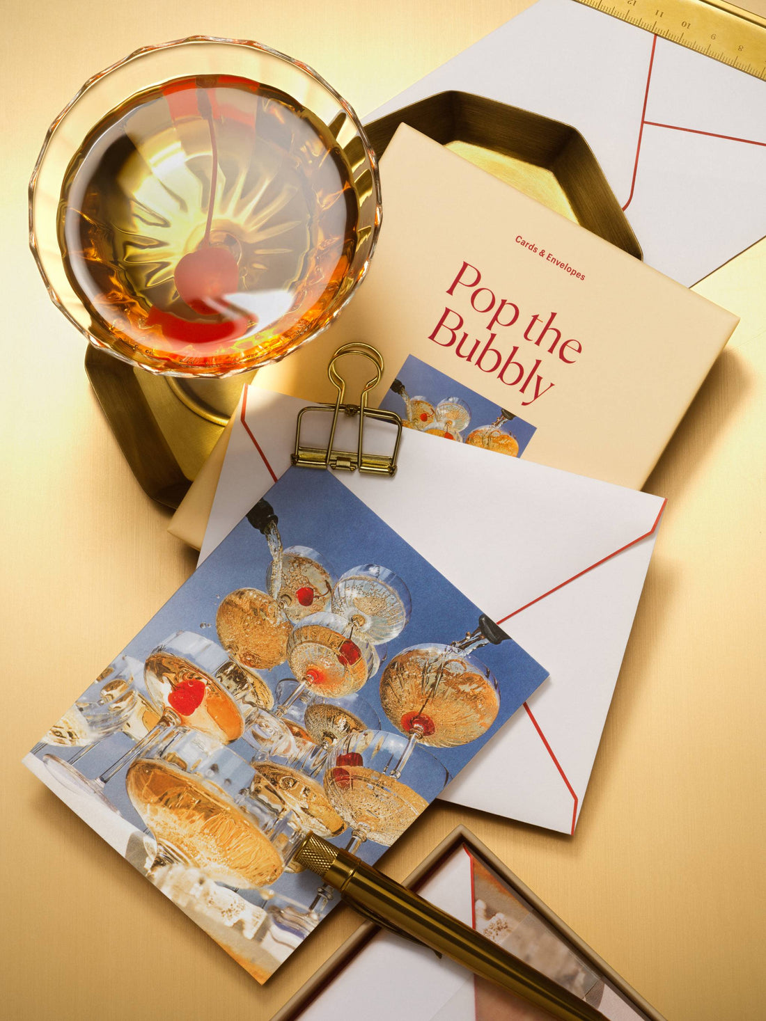 Piecework Pop the Bubbly boxed notecard set with a champagne coupe tower card, cocktail and gold pen on warm gold