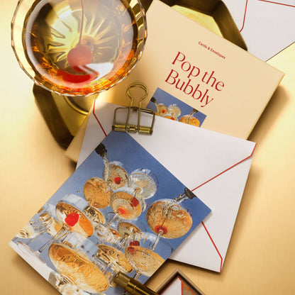 Piecework Pop the Bubbly Stationery Set: peach box and champagne tower notecard with envelope and a cocktail on gold