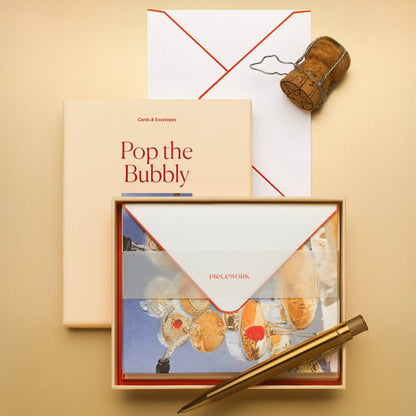 Piecework Pop the Bubbly Stationery Set: peach box and open tray of notecards under a vellum band with a champagne cork