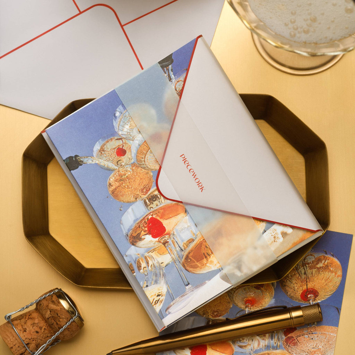 Piecework Pop the Bubbly Stationery Set: champagne tower notecard and envelope on a gold tray with a cork and gold pen