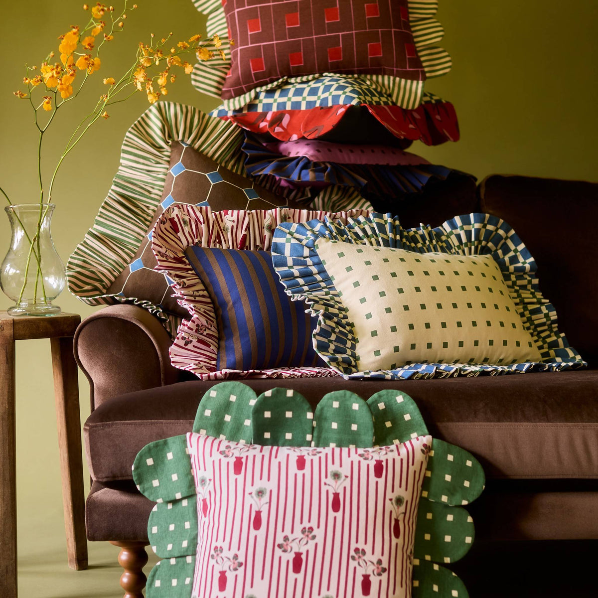 Posie Check Petal Pillow in a stack of Piecework pillows on a velvet sofa