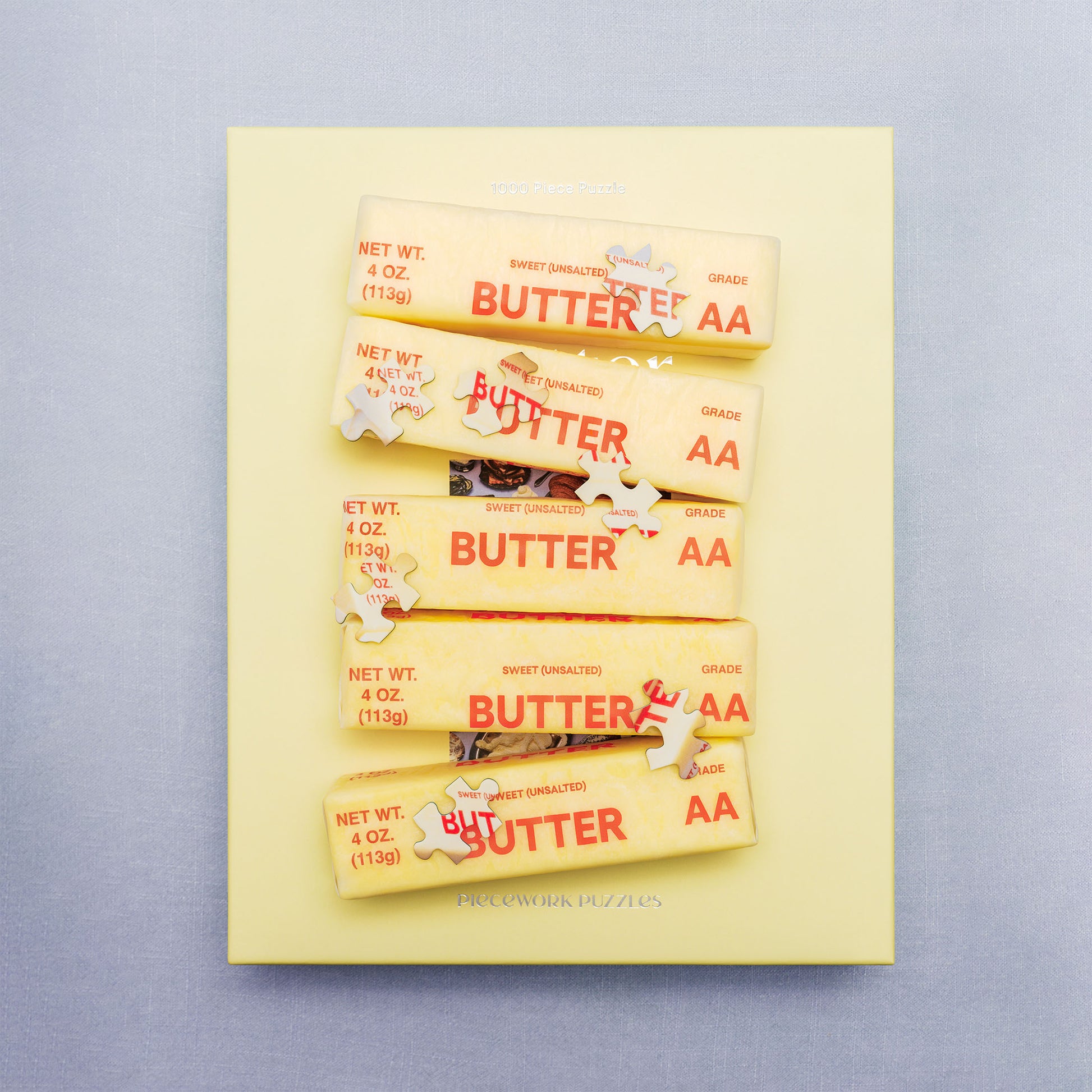 Butter-themed puzzle box obscured by sticks of butter and puzzle pieces of sticks of butter.