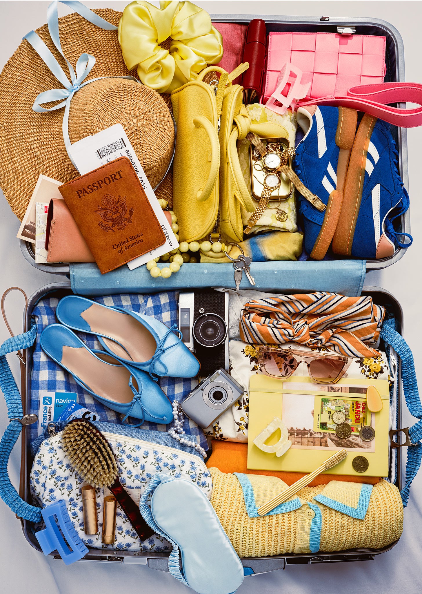 The Bon Voyage puzzle art: open suitcase packed with colorful travel accessories, including blue shoes, a passport, straw hat, sunglasses, camera, yellow sweater, and bright vacation essentials.