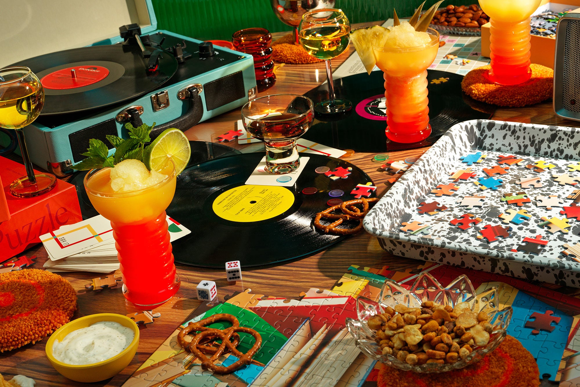 A table scene featuring a record player, cocktails and a puzzle tray filled with puzzle pieces.