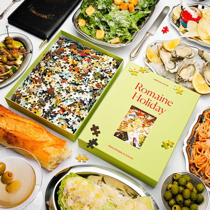 Puzzle box titled 'Romaine Holiday' surrounded by food items on a table.