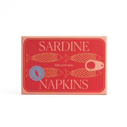 Red and salmon-colored packaging for Sardine Napkins, with graphics resembling a sardine tin, on a white seamless background.