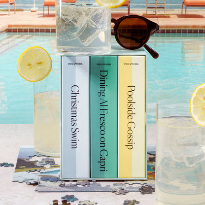 Close-up of the Slim Aarons Trio Set puzzle boxes poolside with sunglasses and lemonade in the scene