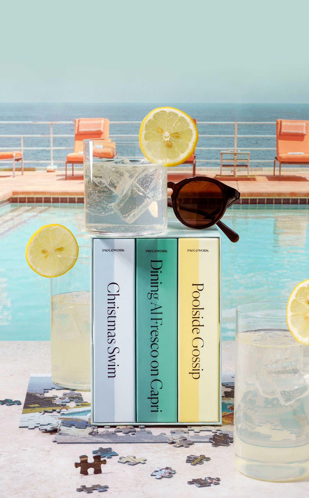 Close-up of the Slim Aarons Trio Set puzzle boxes poolside with sunglasses and lemonade in the scene