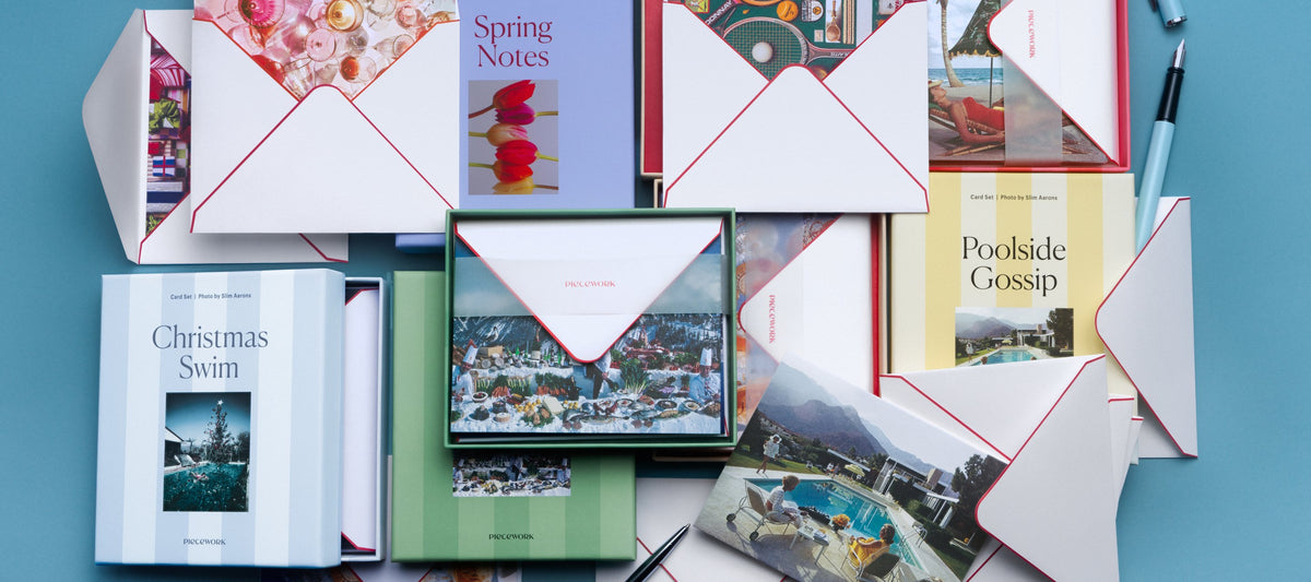 Piecework stationery card sets, including Christmas Swim, Poolside Gossip, and Spring Notes, with envelopes and a pen on a blue background