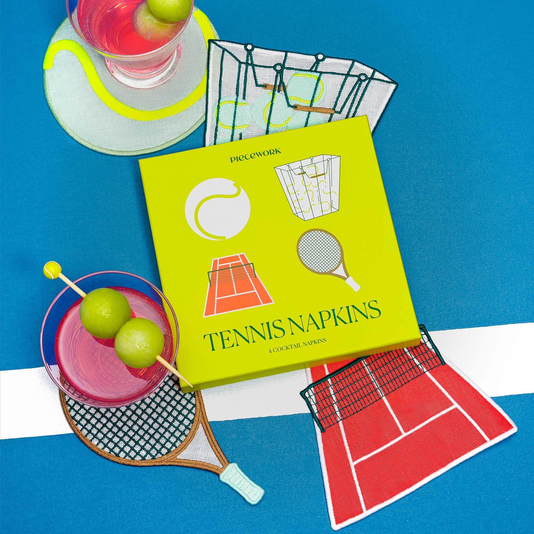 Yellow box of tennis-themed cocktail napkins with drinks on a blue surface.